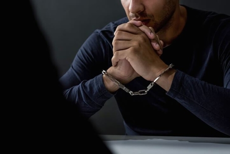 Criminal man with handcuffs in interrogation room
